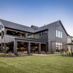 A large, modern black barn-style building with extensive board and batten siding and a covered outdoor patio.