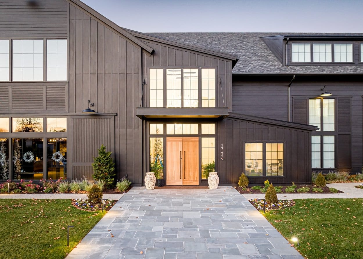 Modern home with dark board and batten siding, large windows, wood double doors, and a landscaped front entrance.