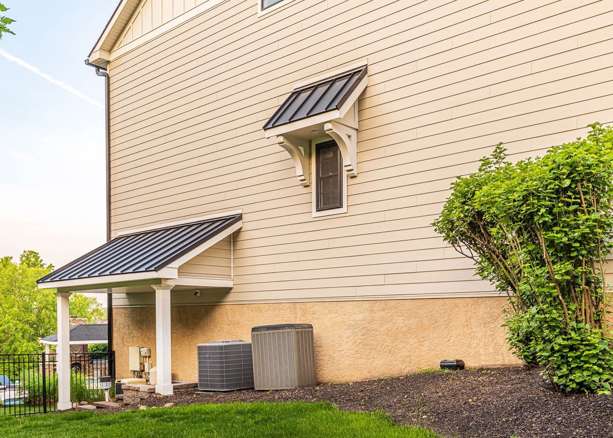 Stucco foundation wall and siding with metal-roofed porch and window flashing details on a home exterior