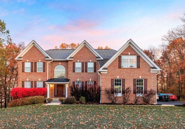 A large red brick home featuring a new front portico with black standing seam metal roofing and white PVC trim as part of a full exterior renovation.