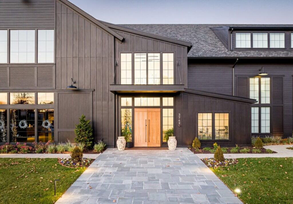 Modern home with dark board and batten siding, large windows, wood double doors, and a landscaped front entrance.