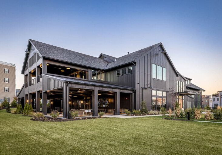 A large, modern black barn-style building with extensive board and batten siding and a covered outdoor patio.