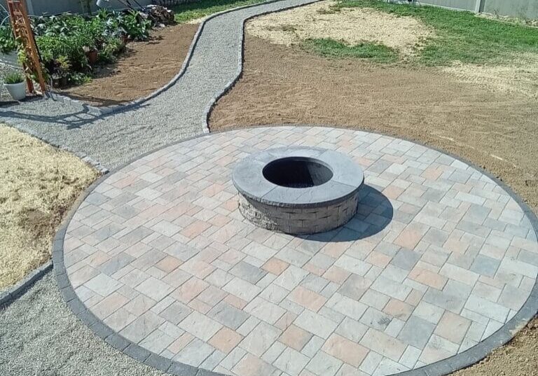 Custom patio with a circular paver design and built-in stone fire pit, bordered by a gravel walkway leading to a garden area in a Mountville, PA.