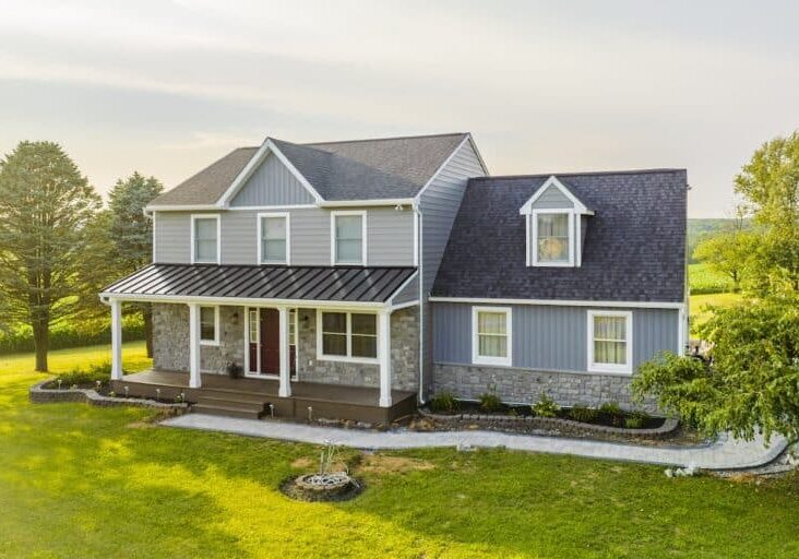 A Coatesville, PA home featuring new siding in light gray, a stone veneer base, a dark metal porch roof, and a custom paver walkway.