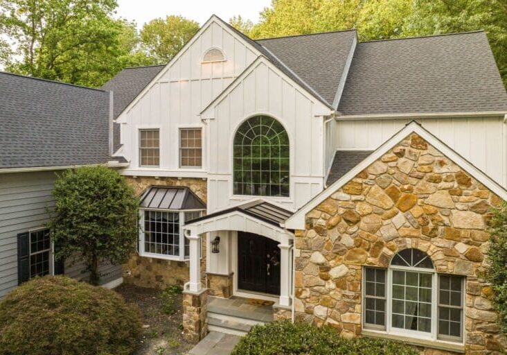 A beautiful home in Chester Springs, PA, featuring white board and batten siding, natural stone veneer, and dark roofing.